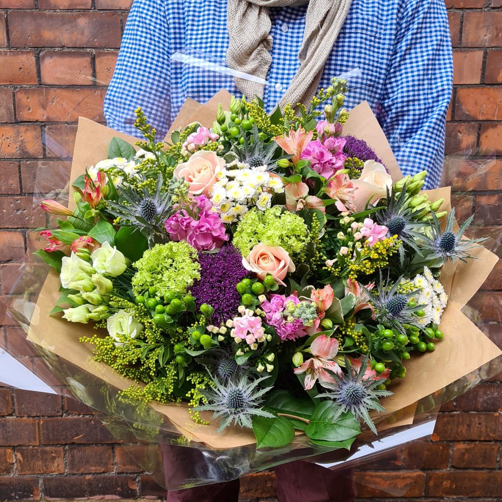 image of a close up of staff members personally designed mothers day bouquet, presented in a wild style in rustic colours.