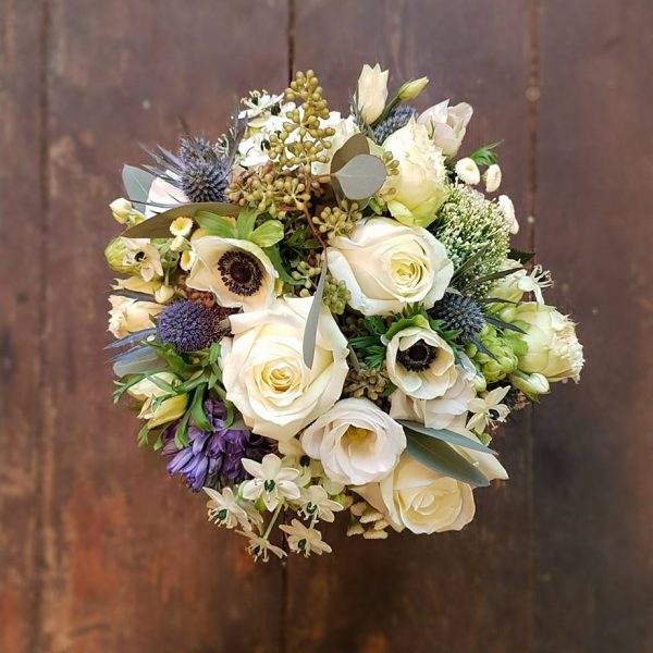 image of a blue and white toned bridal bouquet by Adonis featuring white roses, blue hyacynth and thistle