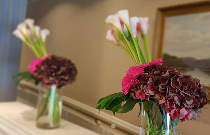 image of 2 corporate arrangements featuring deep red hydrangea and pink cala lilies in stout vases