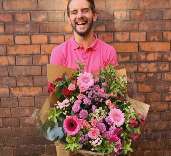 Image of staff member dressed in pink holding a large bouquet